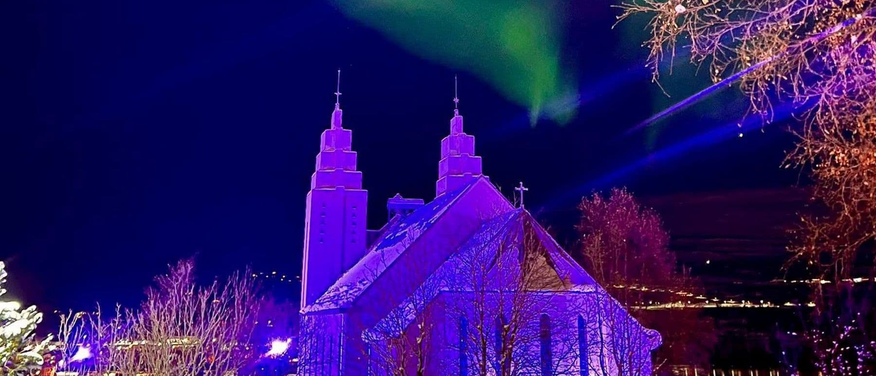 Akureyrarkirkja sveipuð bleikum ljóma undir dansandi norðurljósum.