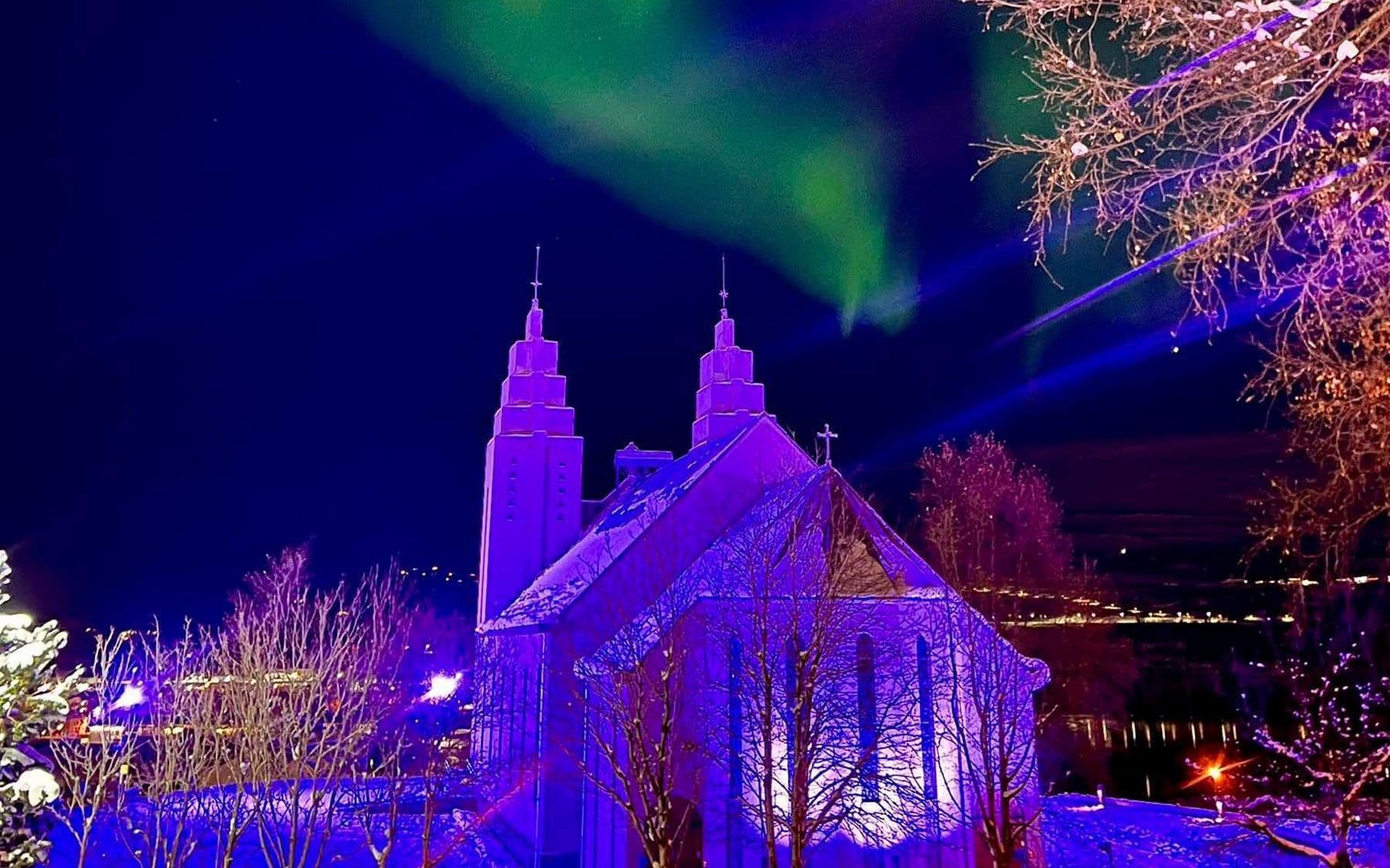 Akureyrarkirkja sveipuð bleikum ljóma undir dansandi norðurljósum.